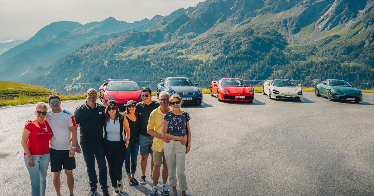 Finding happiness as part of a small, likeminded group. HunterMoss guests pose happily in front of parked supercars in the Alps.