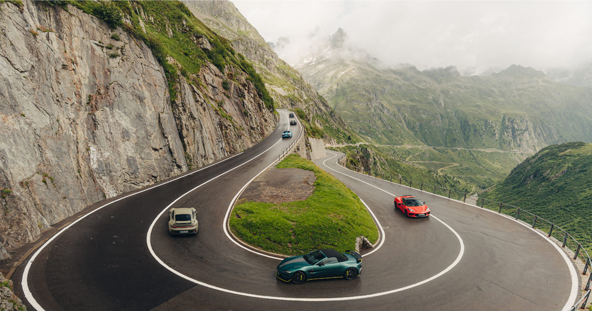 Each corner brings a new vista to enjoy. Supercars navigate a mountain road with lush green and rocky landscape