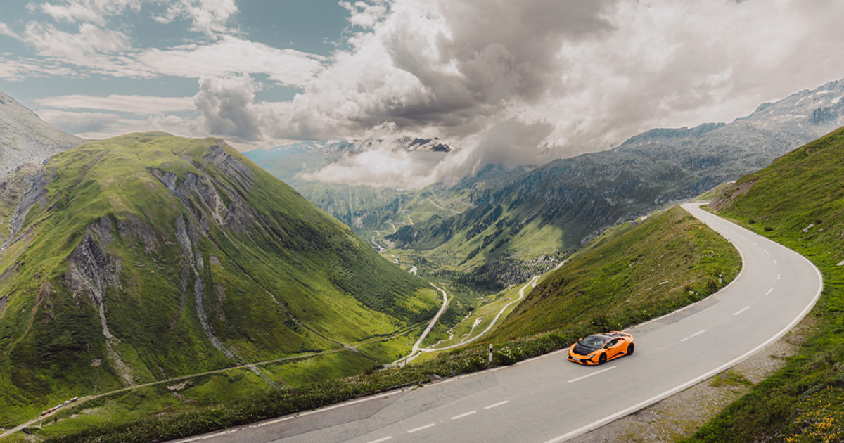 Alpine magic. An orange and black Lamborghini Huracan cruises on a high road above a valley in Europe