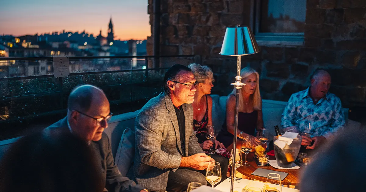 A group of smartly dressed HunterMoss guests conversing on a Florence rooftop during the evening