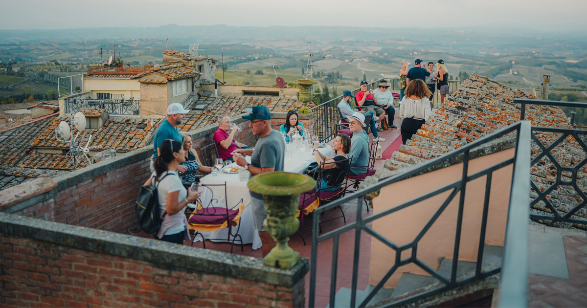 A small group of guests enjoy drinks on a rooftop surrounded by rolling hills