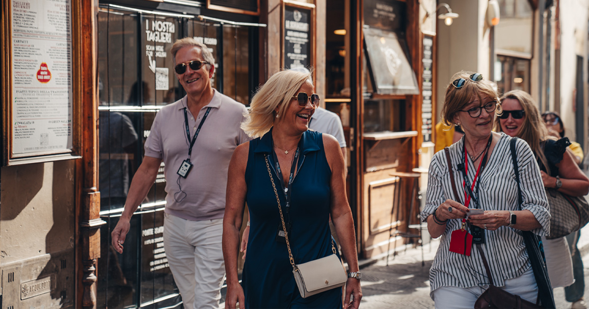 A small group of luxury tour guests smile as they stroll the backstreets of a European city