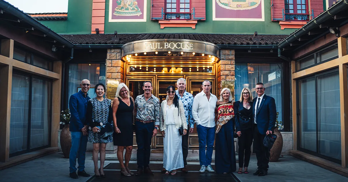 A small group of HunterMoss guests standing happily outside the entrance to Restaurant Paul Bocuse.