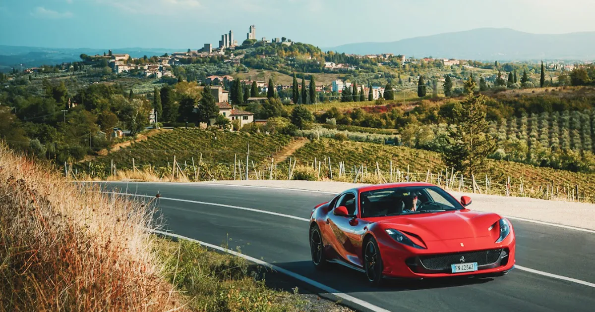 A red Ferrari rounds a vine-covered corner in Tuscany on an HunterMoss luxury adventure.