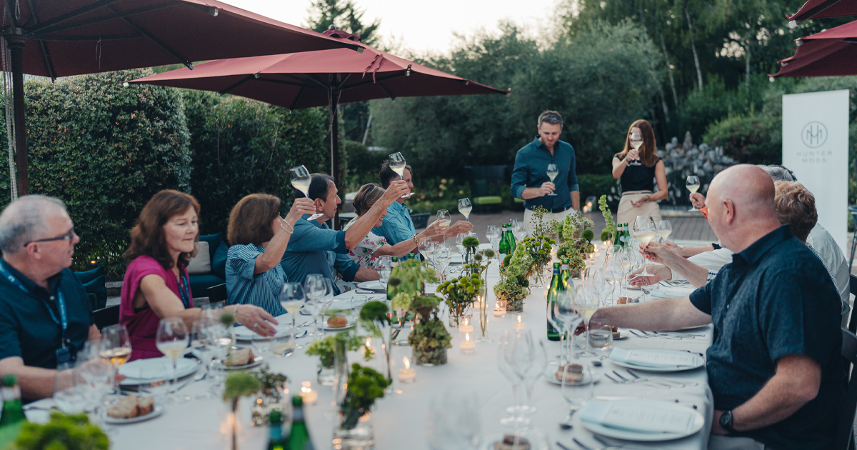 An HunterMoss group toasting at a large dining table in an al fresco setting