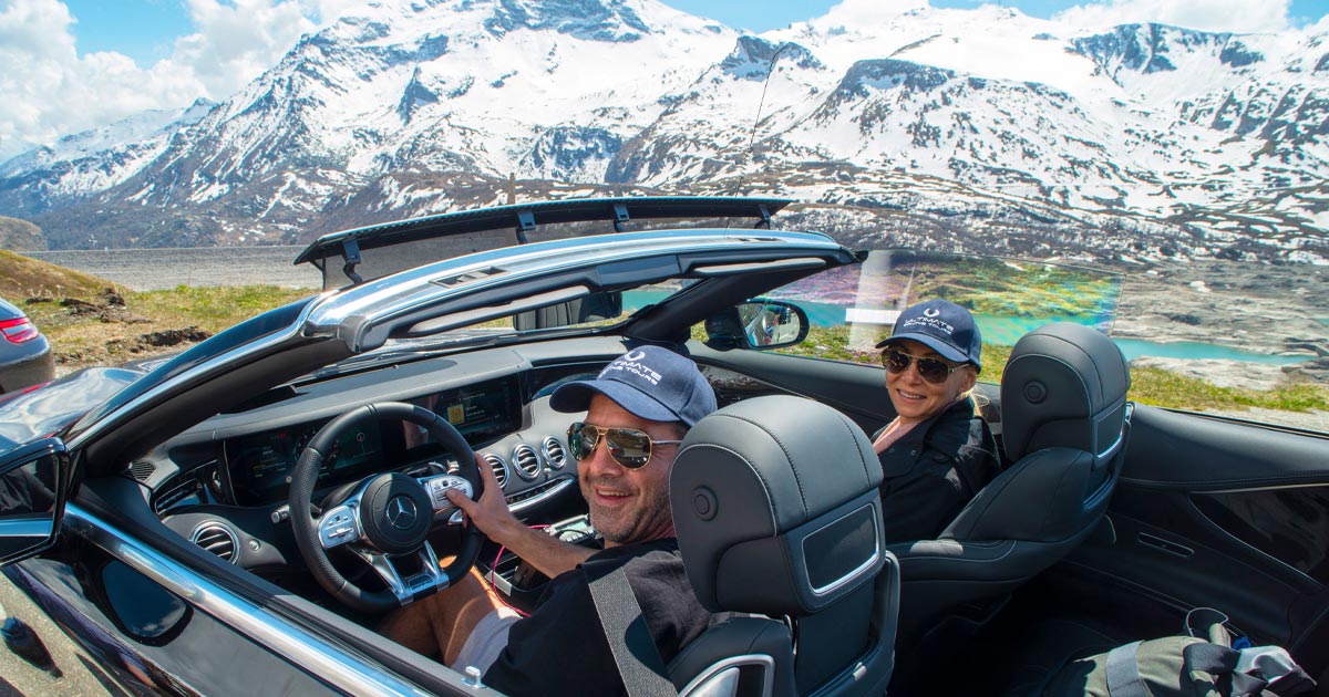 A happy couple decked out in branded hats enjoying a supercar in the Alps with HunterMoss
