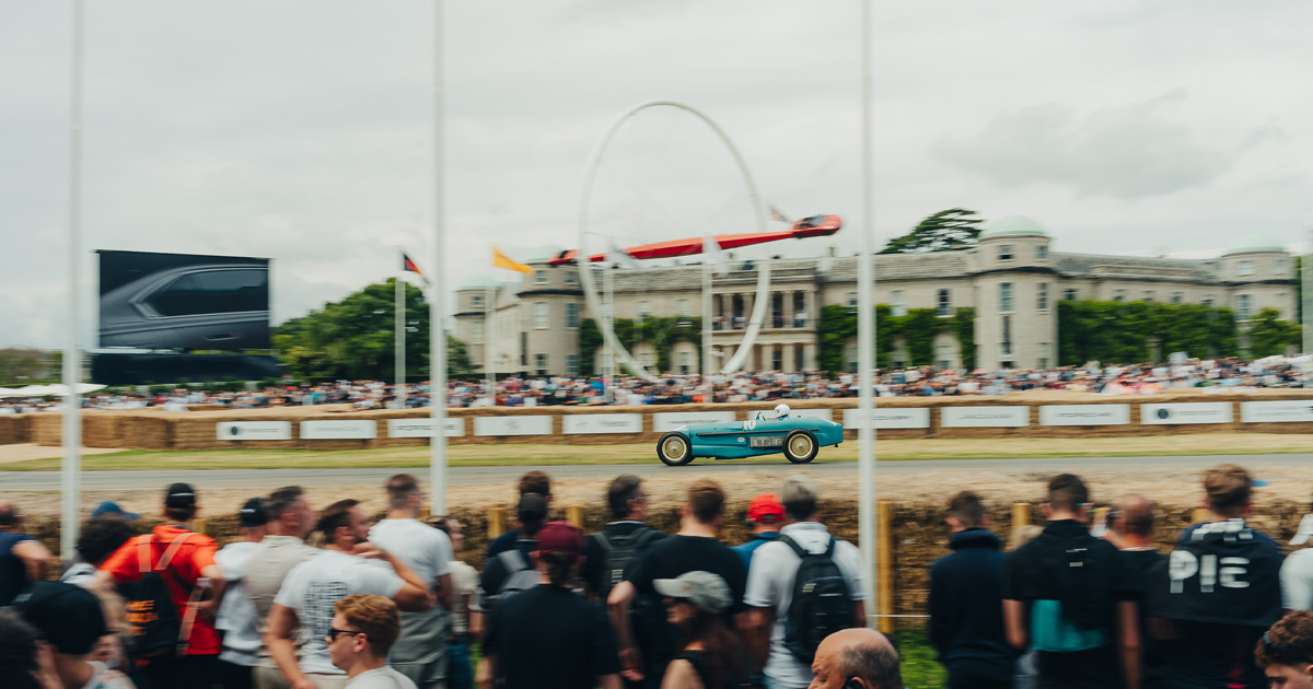 A vintage light blue racing car racing down a straight at Goodwood.