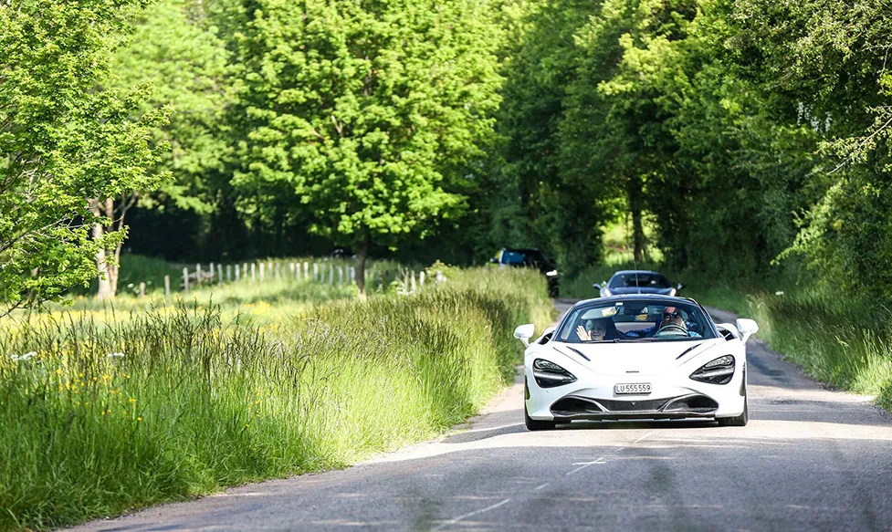 A white McLaren 720S being driven on a green country lane by guests of HunterMoss