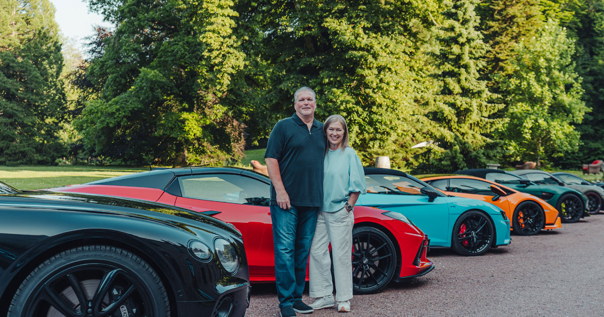 A happy couple pose in front of a lineup of brightly coloured supercars for HunterMoss