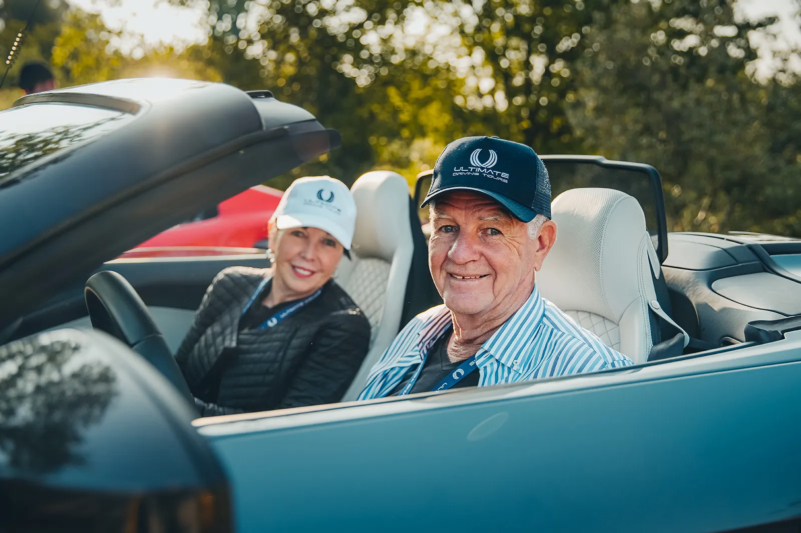 A happy couple wearing HunterMoss branded baseball caps as they drive their convertible supercar