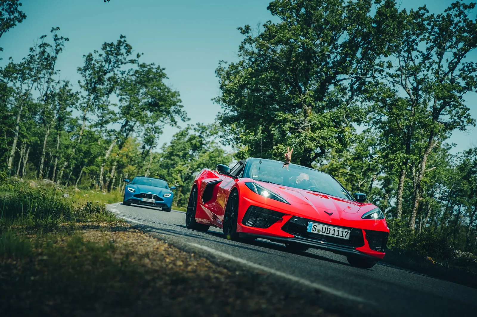 An HunterMoss guest does the peace sign for the camera from their red Chevrolet Corvette on a forest road