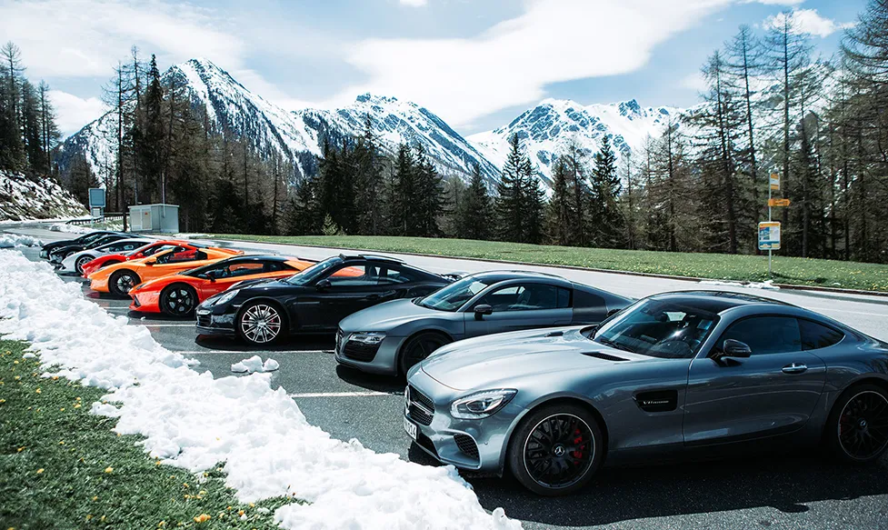 A line of supercars sit in an alpine carpark on an HunterMoss luxury holiday