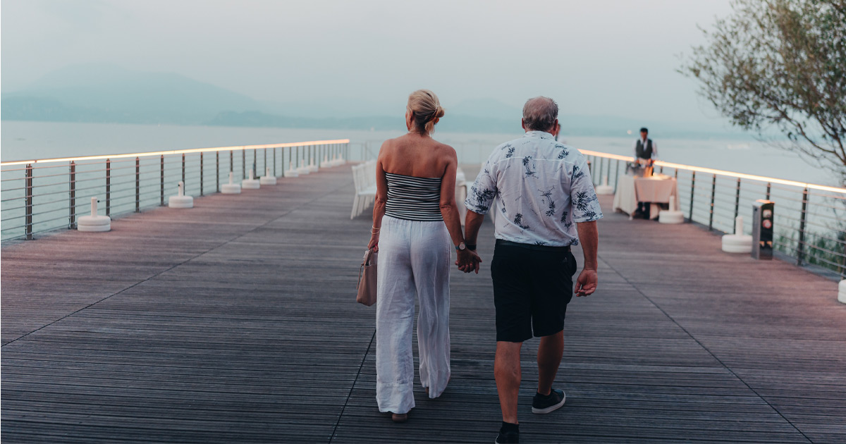 A couple walk hand in hand towards an elegant dining table on a private jetty as a waiter awaits