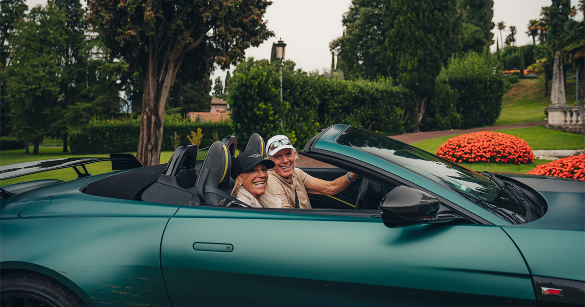 A happy couple wearing baseball caps as they drive a green Aston Martin convertible for HunterMoss
