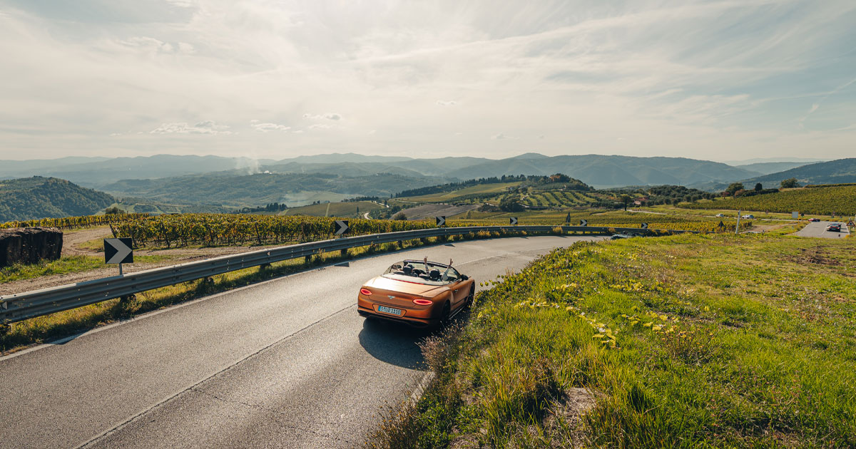 A copper-coloured Bentley Continental GT convertible cruises along a country road on a HunterMoss tour