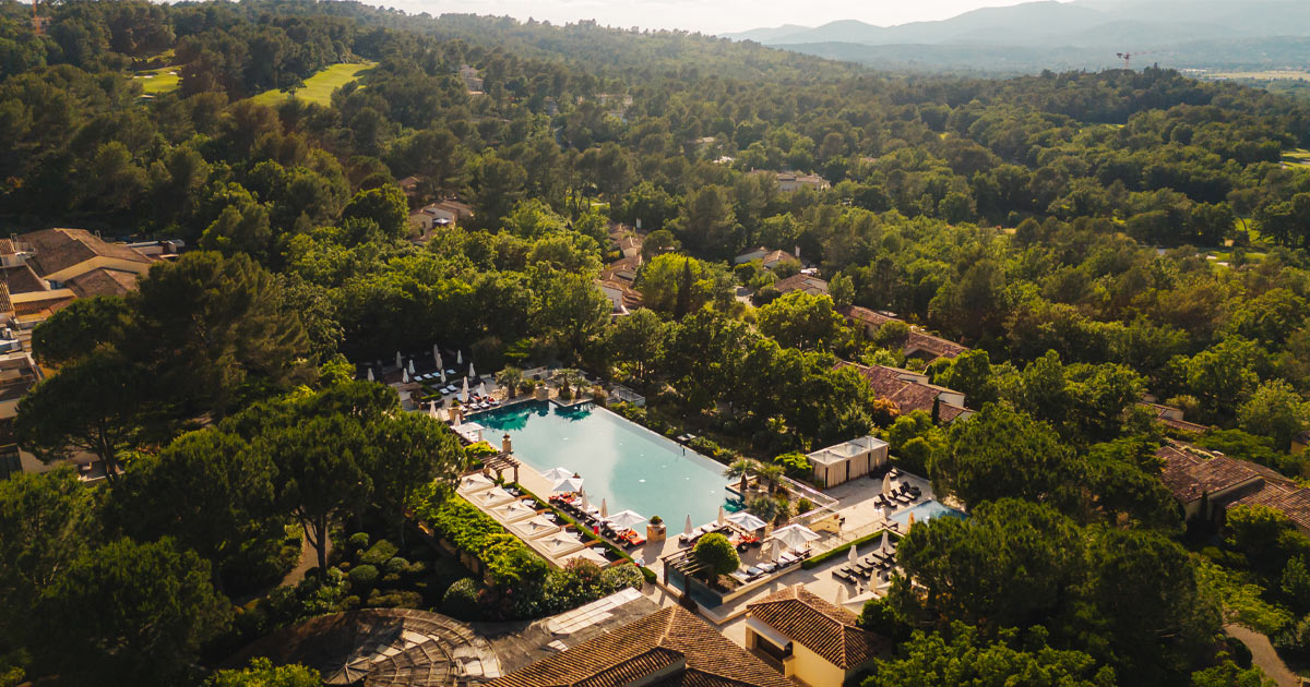 An aerial shot of a large infinity pool at a luxury resort, surrounded by trees and villas
