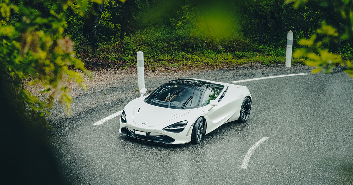 Slick corners are no issue for a car with this level of grip and handling. A white Mclaren 720S turns into a sharp corner on a wet road in a forest
