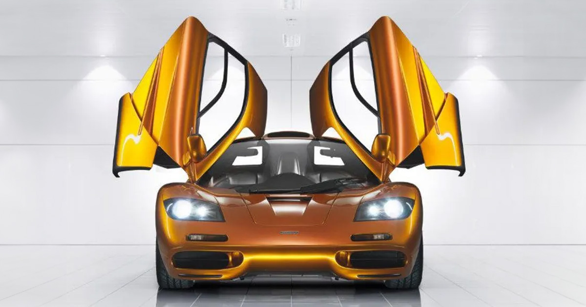 McLaren's engineering prowess is easily seen in these magnificent butterfly doors. A metallic orange McLaren F1 with its dihedral doors open to the sky and its headlights on